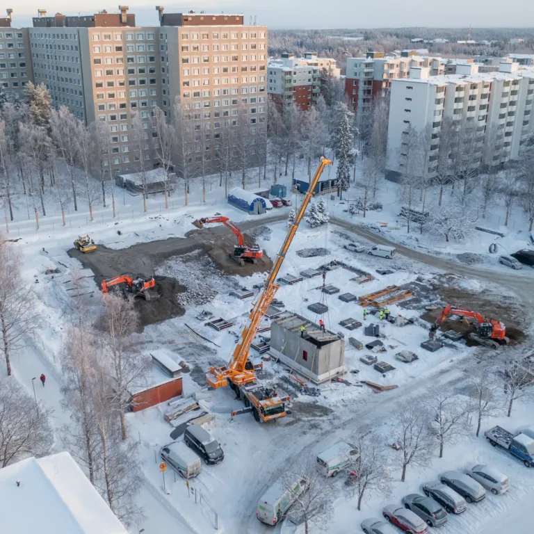 Ilmakuva päiväkodin rakennustyömaasta Hervannan Teräskadulla Tampereella 15.12.2022, nostokurki ja kaivinkoneita lumisella tontilla, esimerkki ammattimaisesta työmaakuvauksesta.